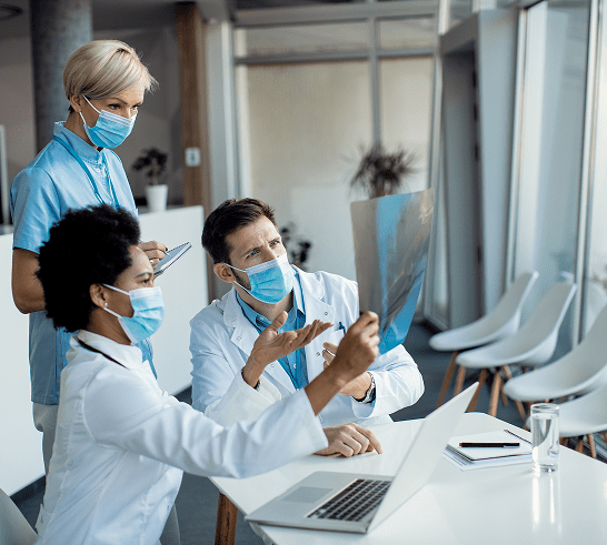 Healthcare professionals in masks are engaged in a discussion with a digital tablet in a modern office setting.
